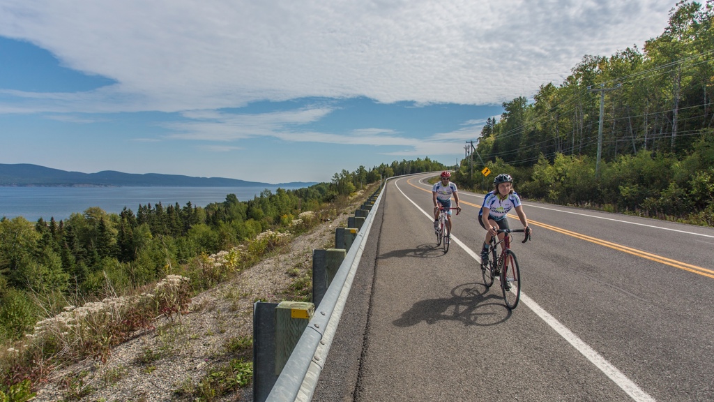 Cyclistes roulant sur une route côtière en Gaspésie avec vue sur le fleuve.